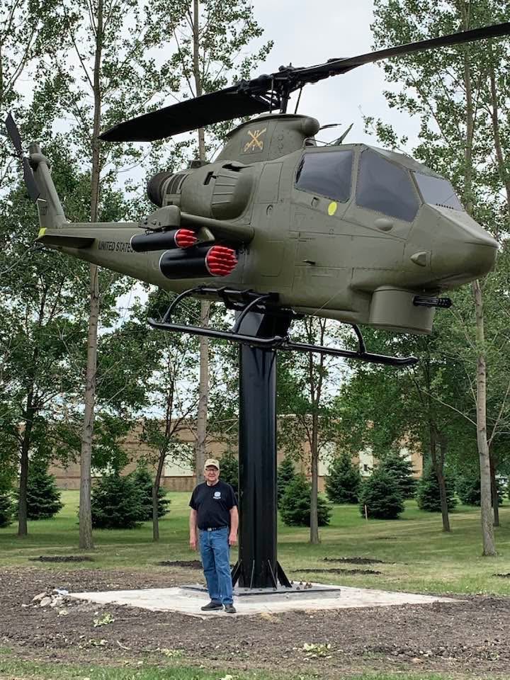 Tom Westcott standing beside the restored 1966 Bell Cobra helicopter at the Martin County Veterans Memorial in Fairmont
