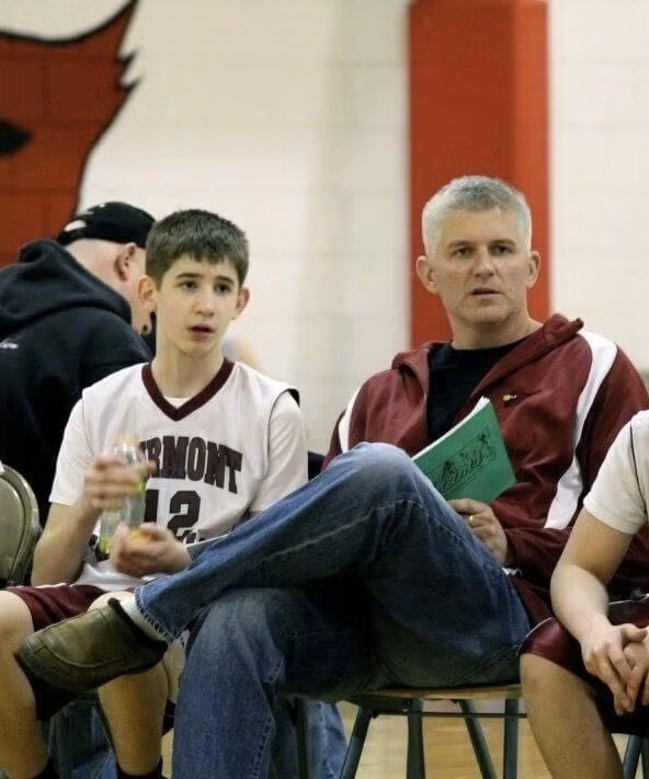 A young Josh Liljenquist seated beside his father, Trent Lee Liljenquist, during a Fairmont basketball game.
