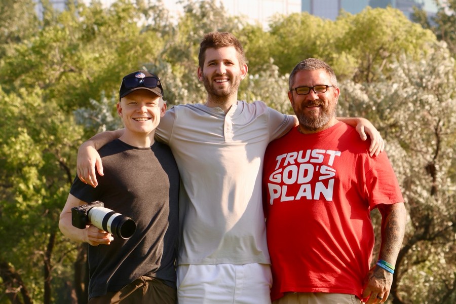 Josh Liljenquist standing outdoors with two filming teammates, one holding a camera