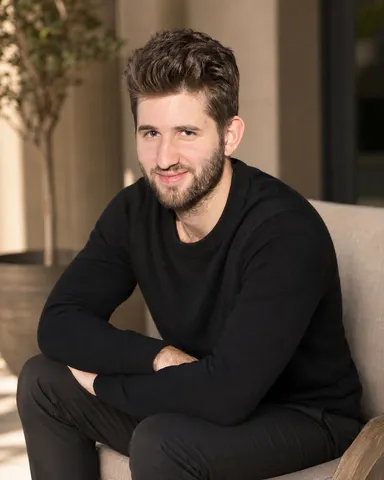 Josh Liljenquist, known online as Joshlilj, leaning forward in an upholstered chair while wearing a black crewneck sweater and dark pants.