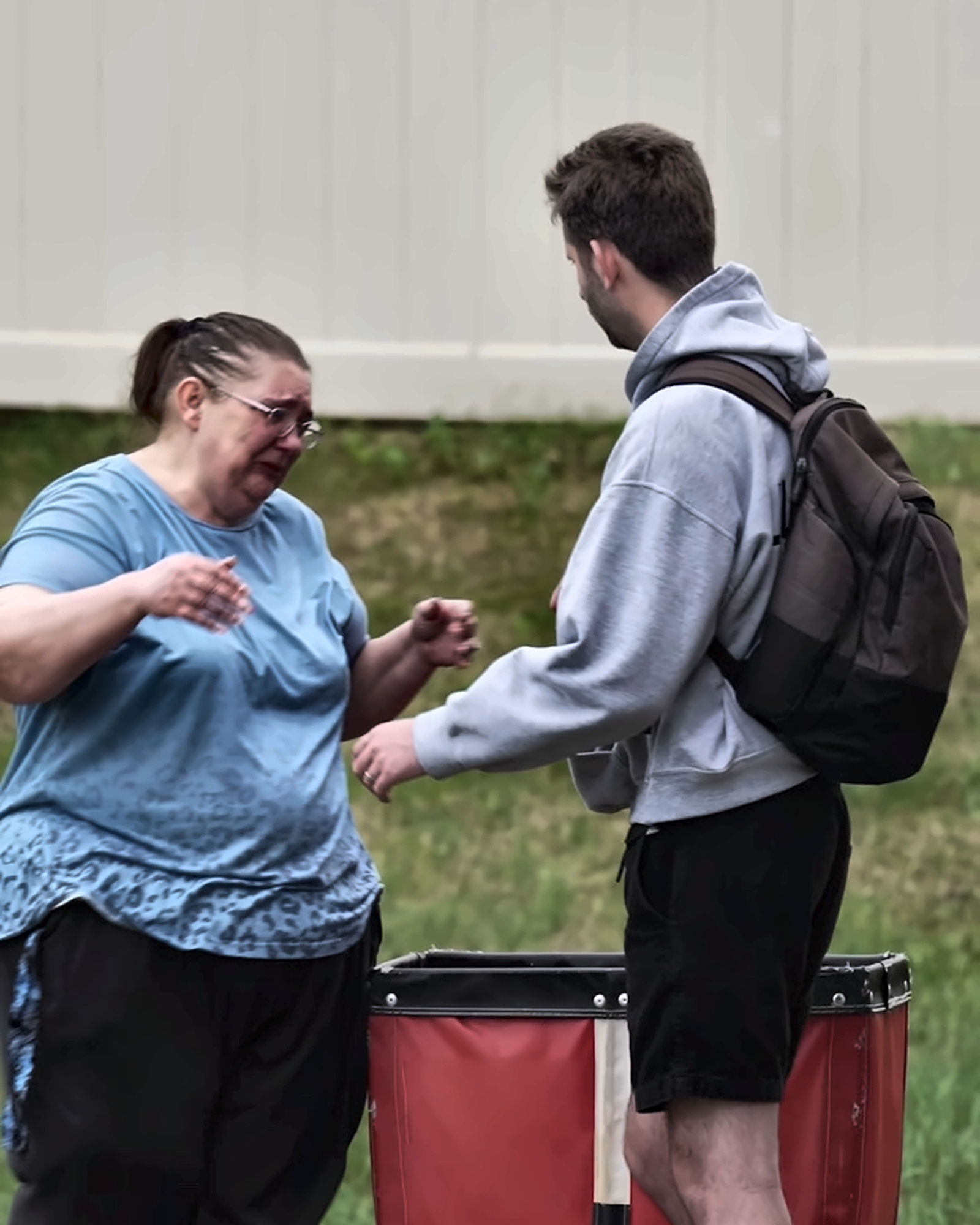 Josh Liljenquist facing a visibly emotional community member beside a red utility cart during an assistance conversation
