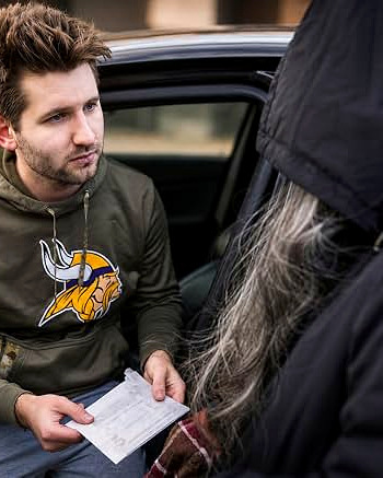 Josh Liljenquist speaking with a community member beside a parked car while holding an envelope