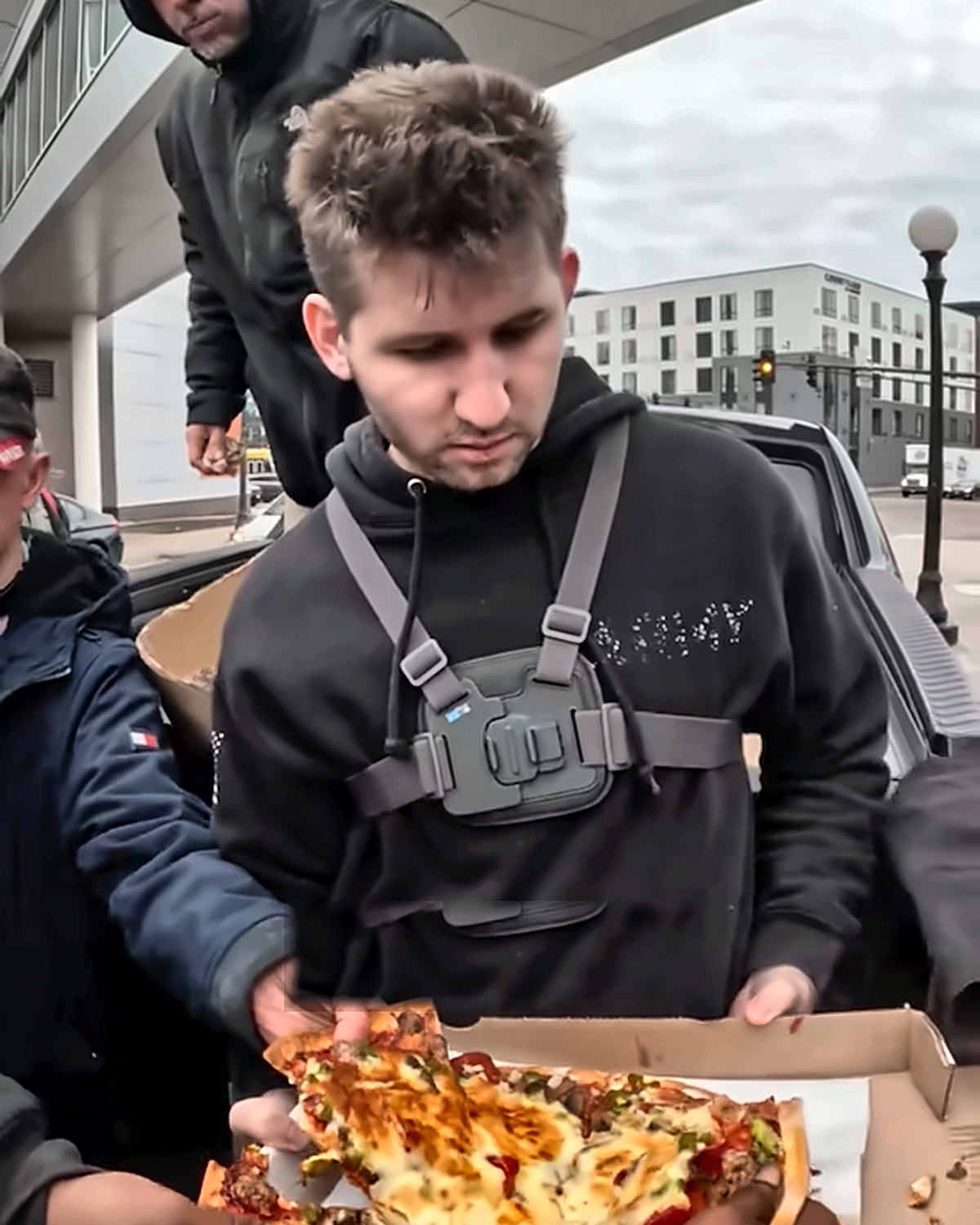 Josh Liljenquist holding a box of pizza while community members take slices during a meal distribution