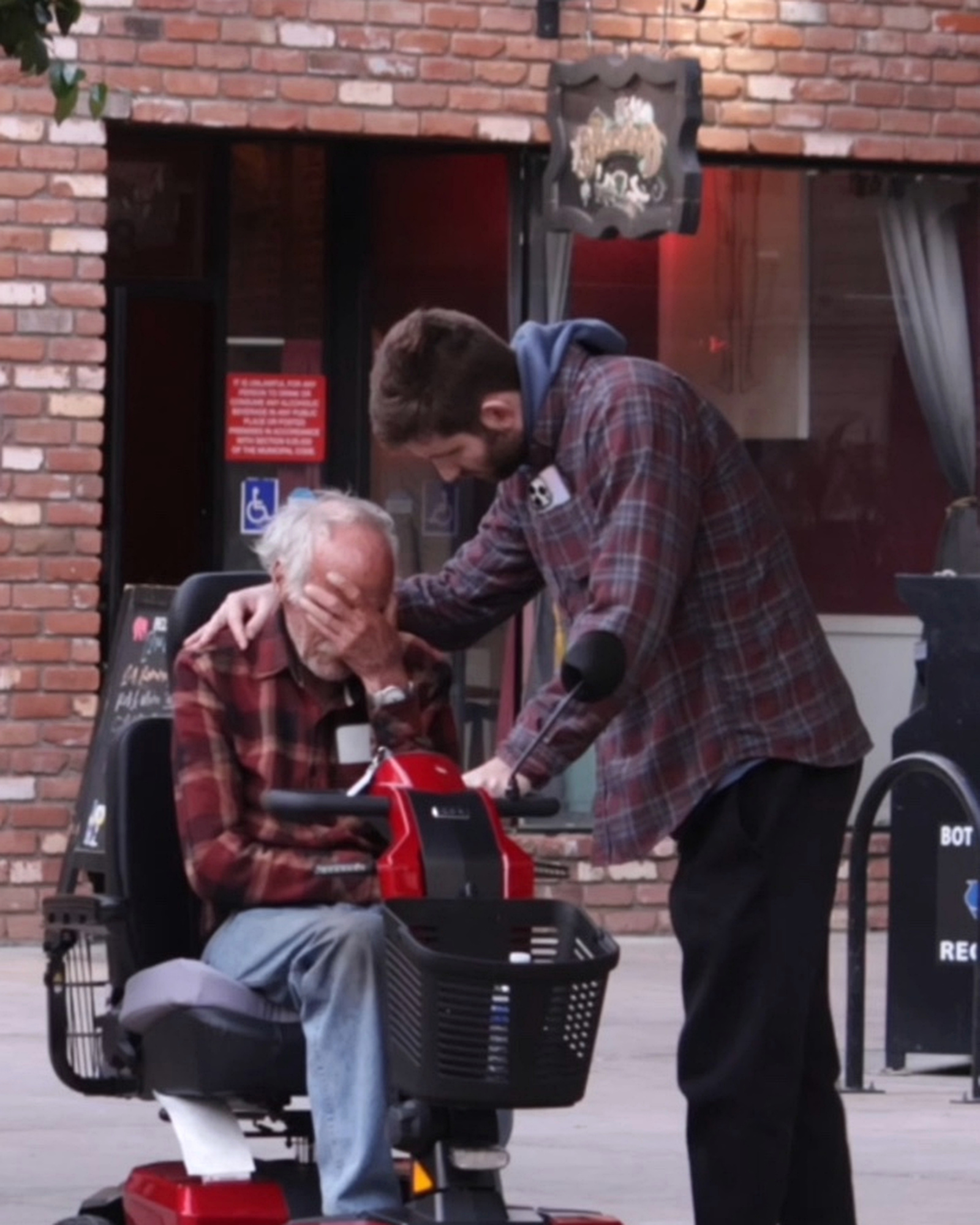 Josh Liljenquist placing a supportive hand on an emotional man seated on a red mobility scooter during an assistance moment