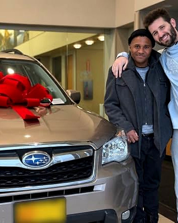 Josh Liljenquist and a community member standing beside a vehicle with a red gift bow