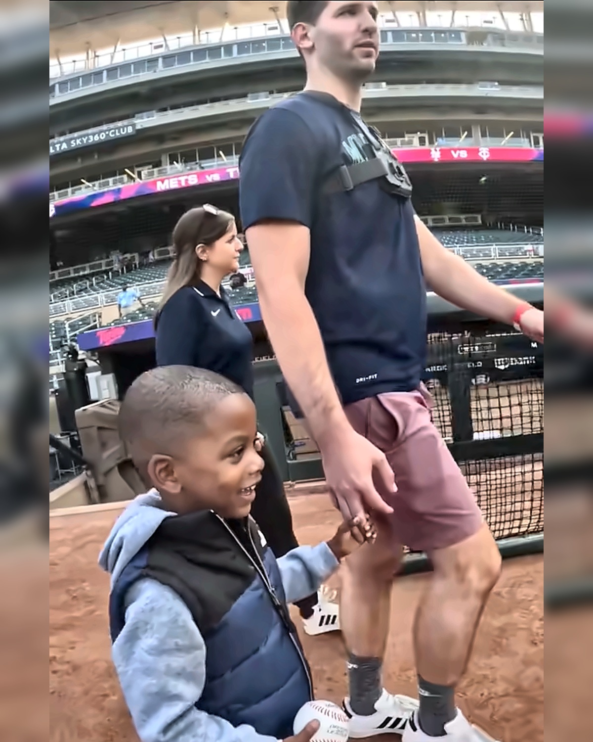 Josh Liljenquist walking beside a smiling child holding a baseball on a professional baseball field